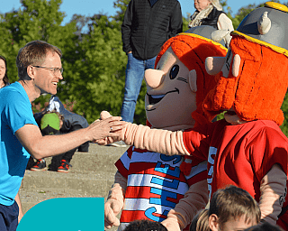 Daniel Günther schüttelt Hände von zwei Maskottchen vor einer Menschenmenge draußen