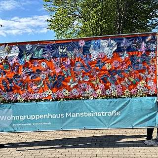 Banner mit bunten Schmetterlingen und Blumen, gehalten von zwei Personen draußen
