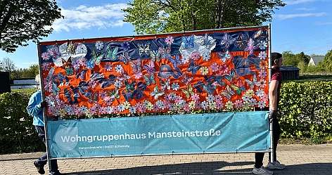 Banner mit bunten Schmetterlingen und Blumen, gehalten von zwei Personen draußen